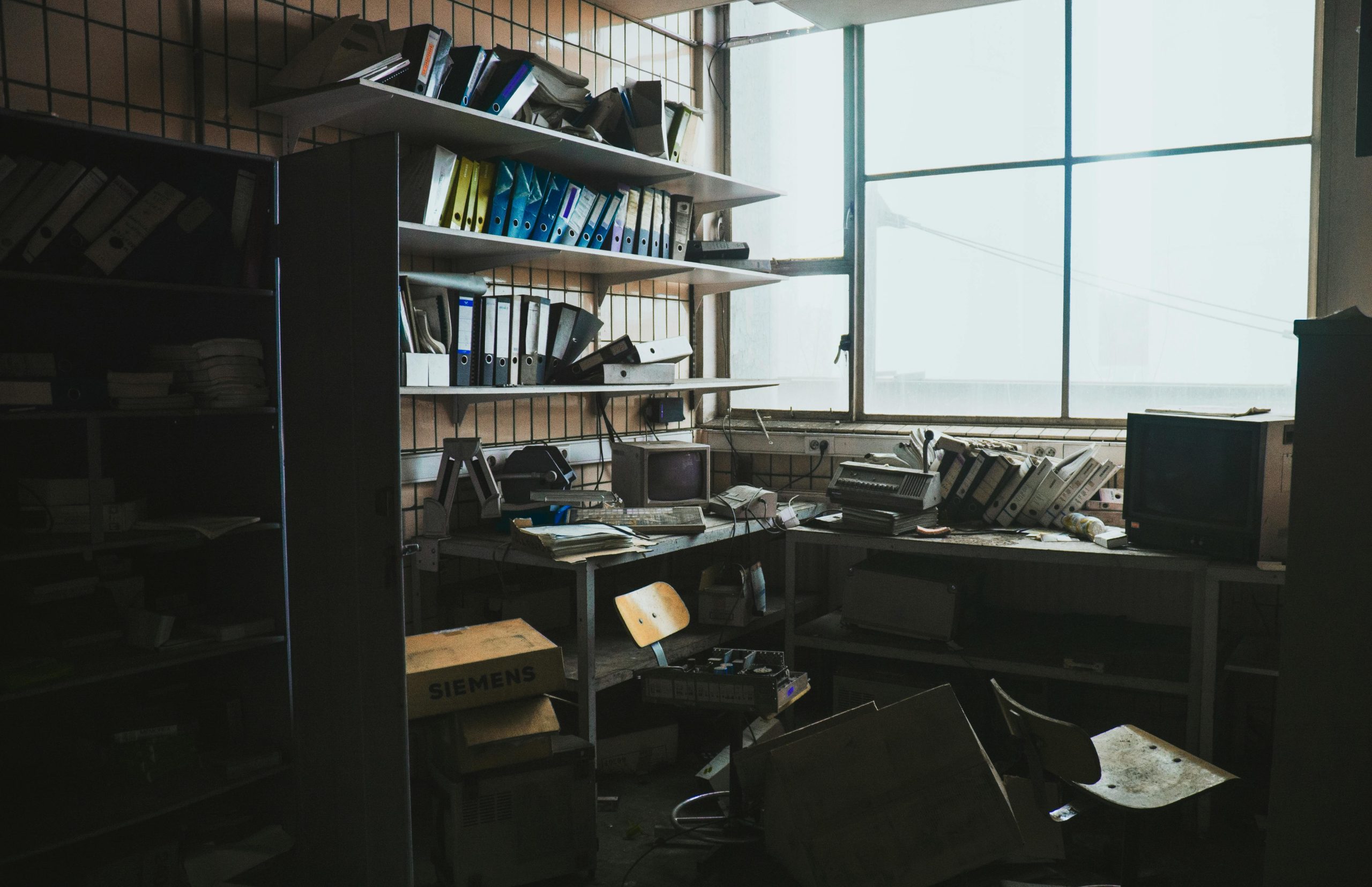 A cluttered, abandoned office space filled with vintage technology and scattered binders.